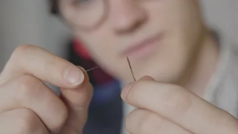 Extreme close-up of male hands threading needle with blurred face of tailor at Stock Footage 137058411