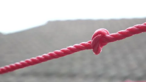 Extreme Close-Up of Red Clothesline Rope Knot Against Blurred Rooftop Background Stock Footage 336983463