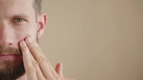 Extreme close-up, serious confident young man 30s, applying facial moisturizer Stock Footage 250659326