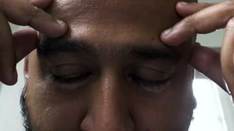 An extreme close up shot of the face of an Asian Indian man massaging his Stock Footage 201183587