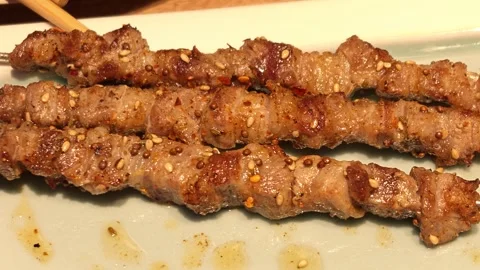 Extreme close-up of three spiced grilled meat skewers resting Vidéo 344853127