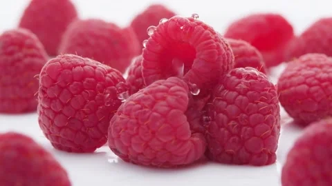 Extreme close up Water drops falling over raspberries lying on white Video stock 165374621