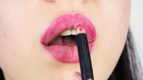 Extreme close-up of young woman's lips. Woman paints her lips with red lipstick. Видео 112956664
