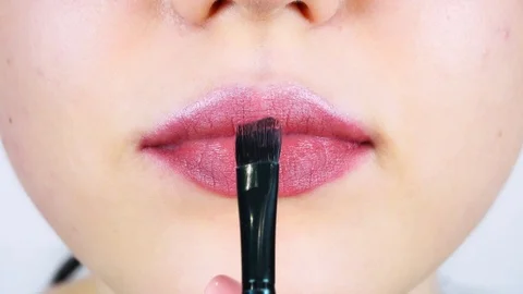 Extreme close-up of young woman's lips. Woman paints her lips with red lipstick. Видео 112956875