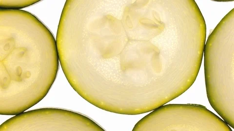 Extreme closeup flat-lay view of young sliced zucchini rotating on white 스톡 동영상 89891469
