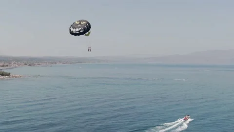 Extreme flying with parachute while speed boat towing near coastline of Stock Footage 160594431