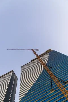 Extreme low angle view of a tall yellow tower crane constructing modern blu.. Stock Photos