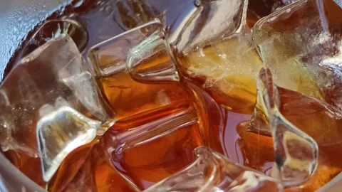 Extreme macro close-up of clear ice cubes floating in amber cold iced beverage Stock Footage 344746825