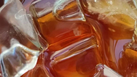 Extreme macro close-up of clear ice cubes shifting slowly in amber whiskey drink Stock Footage 344746826