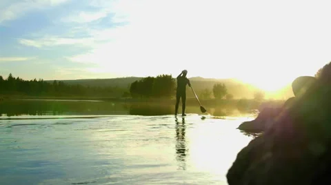 Extreme wide view of Guy paddle boards away into distance Stock Footage 63386212