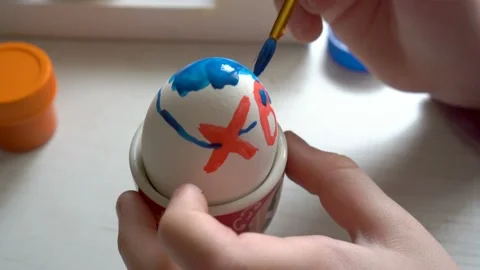 Extremely close-up, the child paints the Easter egg blue and red paint, sitting Video stock 103162093