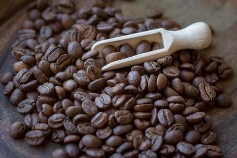 Extremely close-up of coffee beans spilling out of wooden scoop on wooden tab Stock Photos