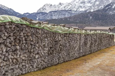 Extremely long woodpile of split logs covered with green tarp Stock Photos