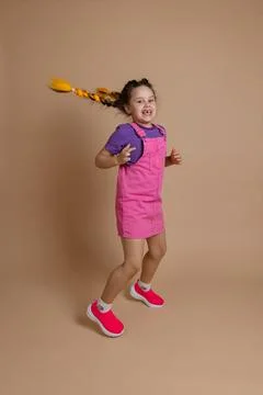 Exuberant active jumping small female kid with two yellow kanekalon pigtails Stock Photos