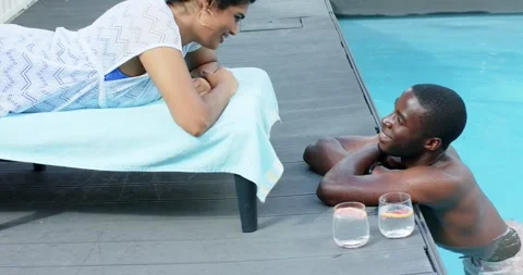 Eye contact sparking Diverse couple exchanging smiles on towel chair and pool Stock Footage 337624933