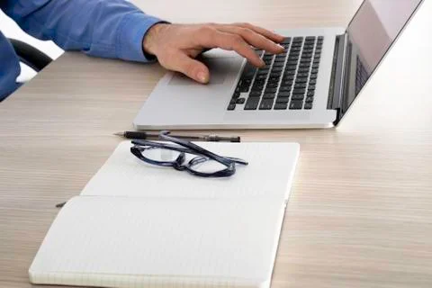 Eye glasses on the open notebook next to computer. Stock Photos