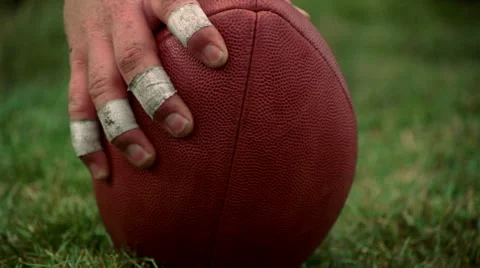 Eye-level close-up of football on turf and hand reaching to tilt it Stock Footage