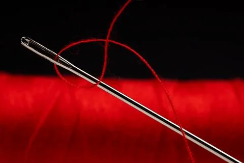 Eye of the needle with red polyester thread. Spool of red polyester sewing th 写真素材