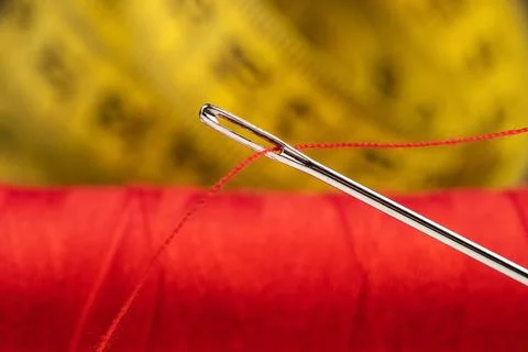 Eye of the needle with red polyester thread. Spool of red polyester sewing .. 写真素材