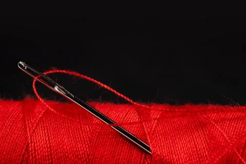 Eye of the needle with red polyester thread. Spool of red polyester sewing th 写真素材