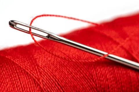 Eye of the needle with red polyester thread. Spool of red polyester sewing th 写真素材