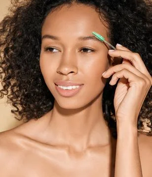 Eyebrow brushing process. Pretty curly woman combing her eyebrows with brush  Stock Photos