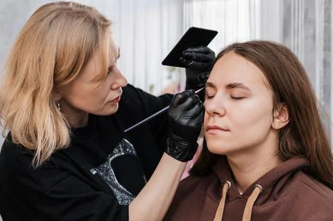 Eyebrow coloring. Close-up, the master applies paint to the eyebrow with a br Stock Photos