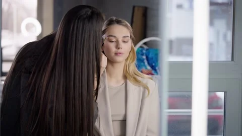 Eyebrow master draws eyebrows with a brush on a young blonde woman in a beauty Stock Footage 236116943
