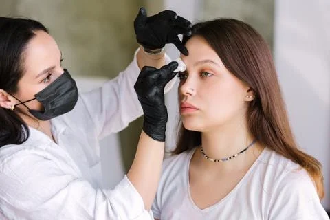 Eyebrow master stands in black clothes in front of the client and prepares for Stock Photos