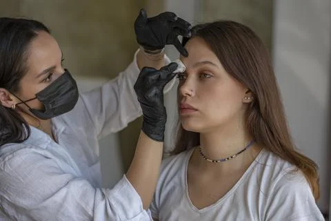 Eyebrow master stands in black clothes in front of the client and prepares for Stock Photos