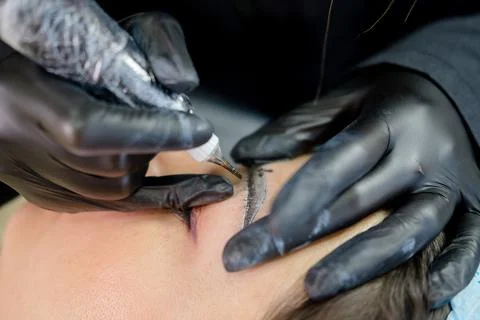 Eyebrow microblading. A master in black gloves holds a blending needle over t Stock Photos