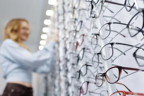 Eyeglass frames on optical store display with customer browsing in background Stock Photos