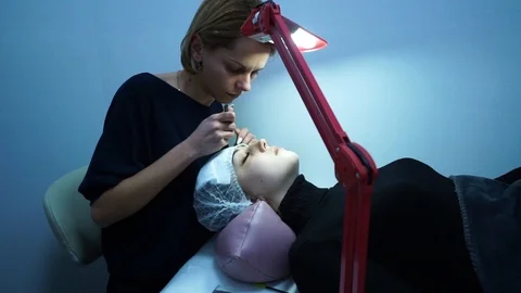 Eyelash extension. Master make-up artist extends eyelashes to a young girl. The Stock Footage 87447219