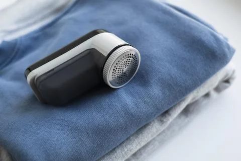 Fabric shaver on stack of sweaters on white background. Stock Photos