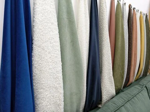 Fabrics of different colors and textures are hanging on a wall in a design st Stock Photos