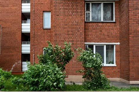 Facade of a brick building with windows and balconies trees grow nearby Stock Photos