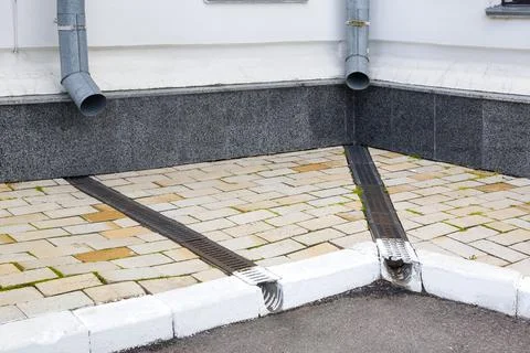 Facade of a building wall with a downspout pipe and a concrete dish canal. Stock Photos