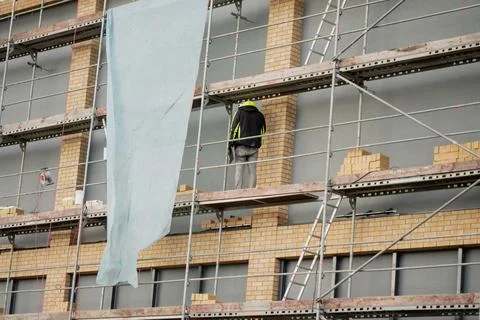 Facade construction with worker scaling scaffolding Stock Photos