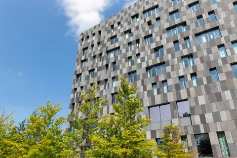 Facade with grey rectangles office building with trees in front Stock Photos