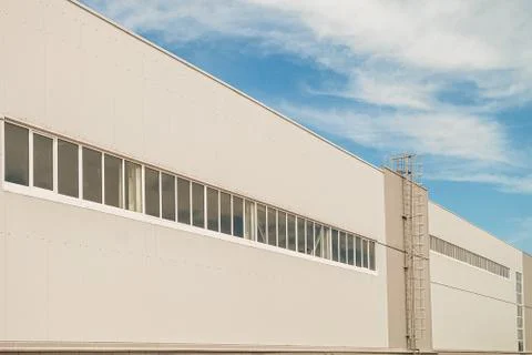 Facade of a long multi-span industrial building under a blue cloudy sky Stock Photos