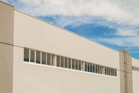 Facade of a long multi-span industrial building under a blue cloudy sky Stock Photos