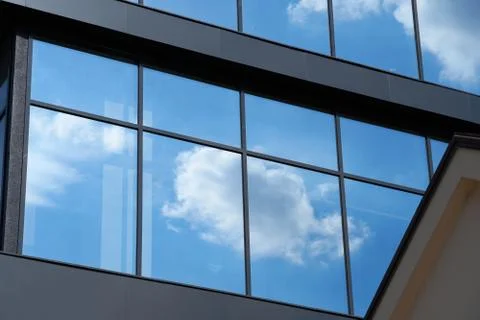 Facade of a modern building on a bright Sunny day, blue sky and clouds reflec Stock Photos