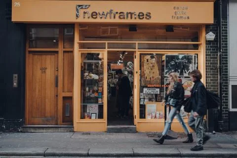 Facade of NewFrames framing shop in Soho, London, UK, people walk past, motio Stock Photos