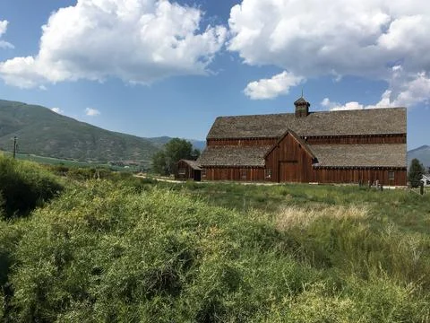 Facade of an old barn in a field surrounded by mountains Stock Photos
