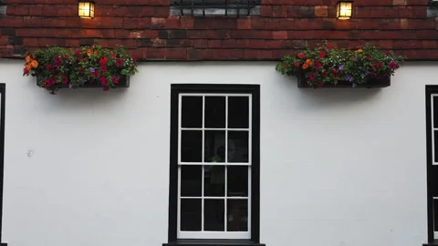 Facade Of An Old House With A White Wall, Black Windows And Flower Pots Stock Footage 307653547