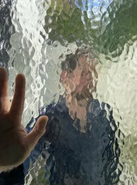 Face and hand in wavy pattern glass window with blurred and distorted face  Stock Photos