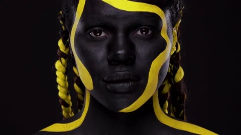 Face art. Woman with black and yellow body paint. Young african