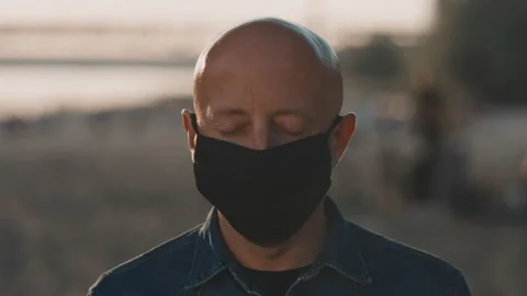 Face of a bald man at the beach during the sunset. He is wearing mask and he is Stock Footage 135405329