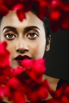 Face of a beutiful female model behind a bunch of red flowers shot in a stu.. Stock Photos