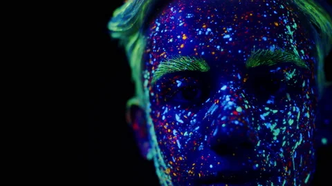 Face of a boy covered in neon paint glowing in ultraviolet light. Young man in Stock Footage 209149979